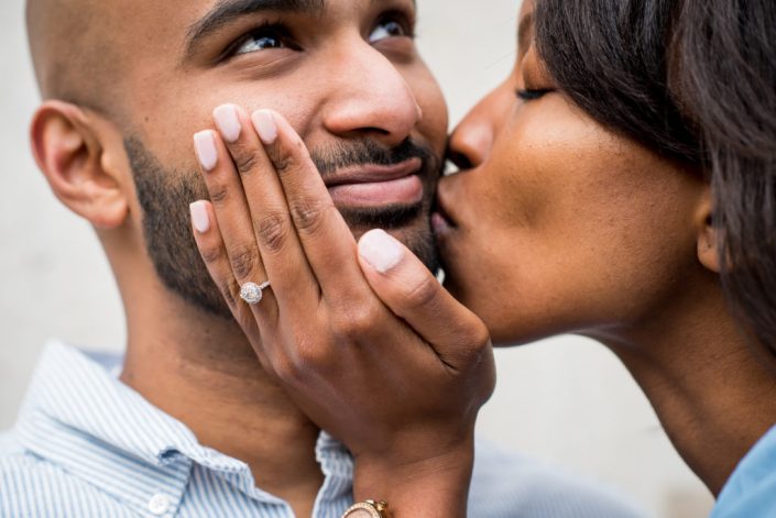 Bride shows her engagement ring off for a photo with a kiss on his cheek