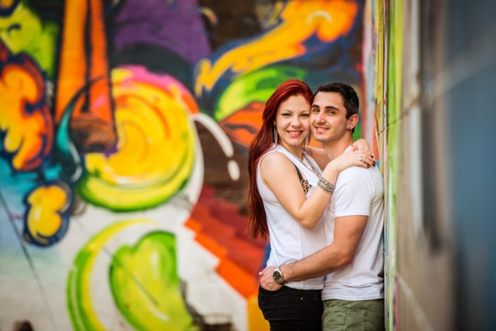 Vibrant hispanic couple pose for engagement infront of colorful wall mural at downtown Richmond Virginia wall mural
