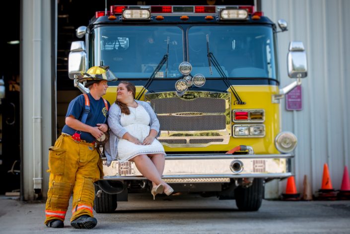 Firefighter poses with bride to be on the front of Goochland Fire truck for engagement photos