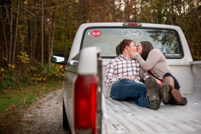 Couple share a kiss in the bed of pick up truck for engagement photos on a dirt road