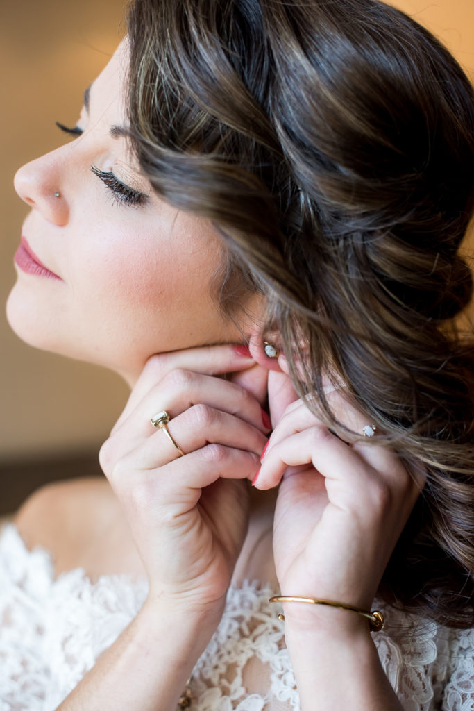 Bride puts on earrings in beautiful window light of hotel room on wedding day in Richmond, VA